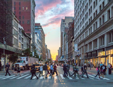 Crowds Of People Crossing An Intersection In Manhattan, New York City With The Colorful Light Of Sunset In The Background