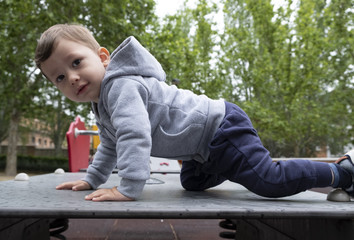 Child under two years playing in the park with a gray jacket and blue pants.