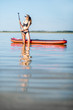 © rh2010 - Beautiful woman in black swimsuit standing with paddleboard in the calm water with reflection during the sunset light