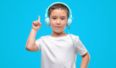 dark haired little child listening music with headphones surprised with an idea or question pointing