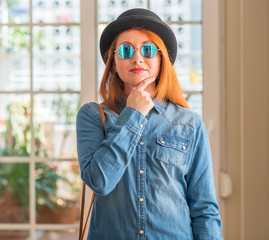 Sticker - Stylish redhead woman wearing bowler hat and sunglasses looking confident at the camera with smile with crossed arms and hand raised on chin. Thinking positive.