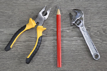 Pliers, wrench and pencil on wooden table close-up