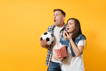 Wall Mural - Young fun cheerful couple, woman man, football fans holding soccer ball, bucket of popcorn, cheer up support favorite team, isolated on yellow background. Sport play family leisure lifestyle concept.