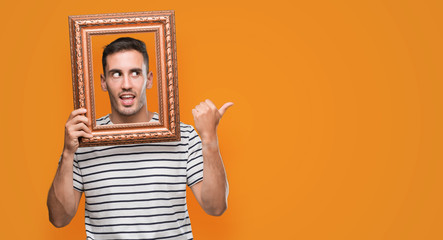 Sticker - Handsome young man looking through vintage art frame pointing with hand and finger up with happy face smiling