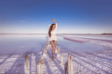 Wall Mural - Beautiful free sexy girl in white swimwear posing on salty beach at sunset. Sensual tanned woman with long healthy hair posing on salt pink lake enjoying nature landscape. Luxury summer vacation.