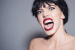 © Volodymyr - Enraged female in black wig screaming, madness concept. Young woman with furious face isolated on gray background