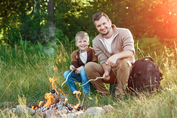 Wall Mural - Father and son by the fire against a background of green nature. Hike, time with family, family life, outdoor recreation.