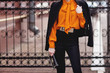 © Sviatlana - Street, office, bright style. Young woman, business style, black jacket, black pants, black handbag, sunglasses, orange blouse, belt, bracelet. Details.