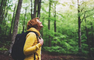 smiling tourist traveler with backpack into road at summer green forest, girl hiker in yellow hoody 