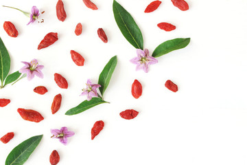 Closeup of Goji berries, Lycium barbarum. Dried Asian fruit, leaves and blossoms isolated on white wooden background. Healthy superfood. Floral pattern, decorative corner. Flatlay, top view.