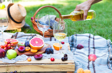 Wall Mural - Picnic background with white wine and summer fruits on green grass, summertime party