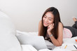 © weedezign - Asian woman wear pink vest laying on bed browsing  data on laptop in bedroom in morning.work at home.e-larning concept.study online.