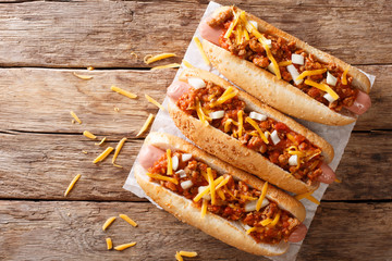 Traditional American chili hot dogs with cheddar cheese, onion and spicy sauce closeup. Horizontal top view