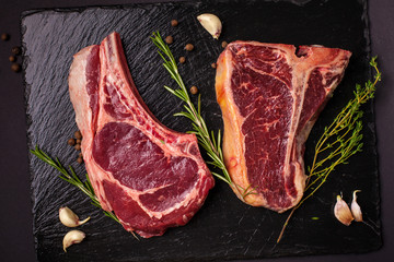 two large pieces of a mutton raw steak, pork, veal, beef lie on a black kitchen slate on a black background, a knife and fork next. copy space, top view