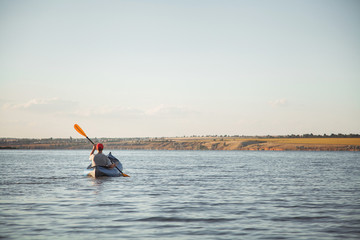 A young man is riding a kayak. Quiet waters and bright sun.