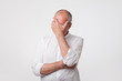 Displeased mature man in white shirt covering his face with hand over gray background.