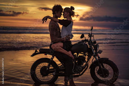 Fotografie, Obraz passionate couple cuddling on motorcycle at beach during sunset