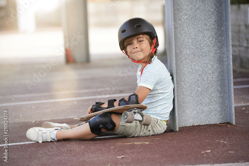 Fototapeta Young boy with skateboard sitting on the ground