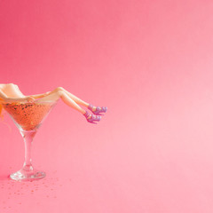 Wall Mural - Doll bathing in martini glass full of gold glitter on pink background. Creative minimal beauty summer concept
