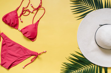 Beach apparel and tropical palm leaves arranged on yellow background