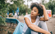 Attractive Afro American woman sitting on bench outdoors in the park feeling dissapointed aftre conversation with friend. Dark-skinned female sitting in the park relaxing. People, emotion, lifestyle