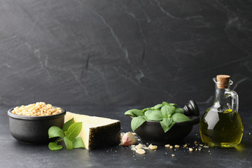 Wall Mural - Basil leaves, parmesan cheese, pine nuts, garlic and olive oil on black stone background. Pesto sauce ingredients.