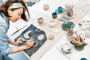 Close-up view of a female potter making and molding clay dishware in a workshop using different tools