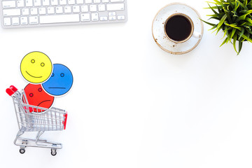 Poster - Client feedback concept. Emoji smiling, neutral, sad face near shopping cart on work desk on white background top view space for text