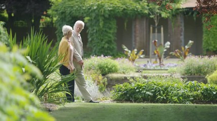 Wall Mural - Senior romantic couple walking through beautiful gardens, in slow motion