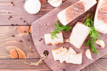 Sliced salted lard with garlic and dill on a cutting board on a wooden table. Top view