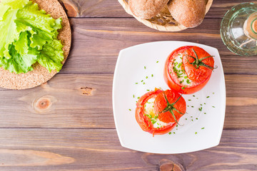 Fresh tomatoes baked with cheese and egg sprinkled with green onions on a plate on a wooden table. Top view. Copy space