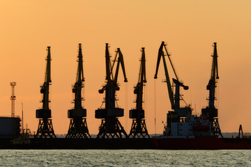 Silhouettes of port cargo cranes at sunset sky background