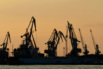  Silhouettes of port cargo cranes at sunset sky background