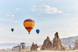 Fototapeta  - Woman in a long dress on background of balloons in Cappadocia. Girl with flowers hands stands on a hill and looks at a large number of flying balloons. Turkey Cappadocia fairytale scenery of mountains