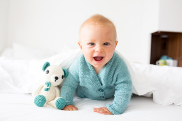 Wall Mural - Little cute baby boy, child in knitted sweater, holding knitted toy, smiling happily at camera