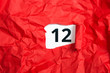 rotes zerknülltes Papier, aufgerollt mit Zahl zwölf - 12 auf weißem Untergrund