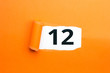 Zahl zwölf - 12 verdeckt unter aufgerissenem orangen Papier