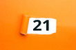 Zahl einundzwanzig - 21 verdeckt unter aufgerissenem orangen Papier