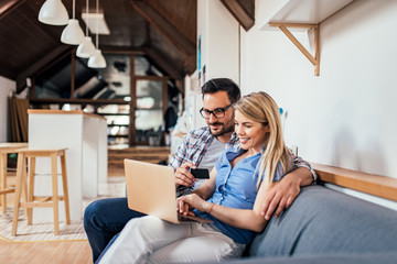 Couple shopping online while sitting on the sofa in modern apartment.