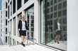 © Westend61 - Smiling businesswoman with newspaper walking in front of office building