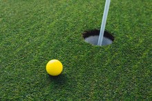 Yellow Golf Ball Nearby Hole With Pin Flag, Green Grass Background, Closeup View