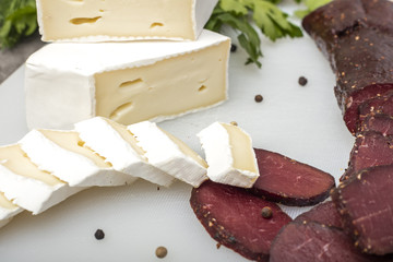 Poster - Soft cheese with white mold and dried meat on a cutting board