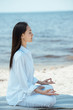 © LIGHTFIELD STUDIOS - side view of young asian woman in ardha padmasana (half lotus pose) on yoga mat by sea