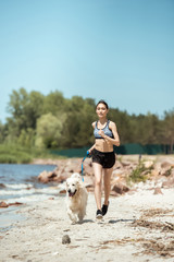 Wall Mural - female athlete jogging with dog on beach during daytime