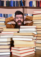 Leinwandbilder - Scientific discovery concept. Teacher or student with beard wears eyeglasses, sits at table with books, defocused. Man on shocked face between piles of books in library, bookshelves on background.