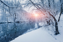 Winter Forest On The River At Sunset. Colorful Landscape With Snowy Trees, Frozen River With Reflection In Water. Seasonal. Snow Covered Trees, Lake, Sun And Blue Sky. Beautiful Forest In Snowy Winter