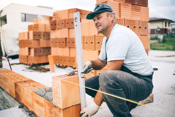 professional construction worker laying bricks and building house in industrial site. Detail of hand adjusting bricks