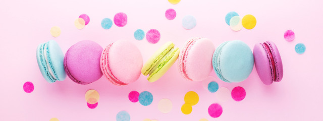 The row of colorful sweet macarons on pink background decorated with confetti. Top view, minimal, banner.