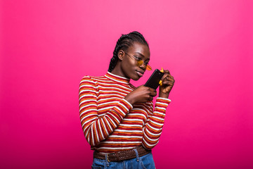 Wall Mural - Beauty happy african woman looking at phone and writing message isolated pink background.