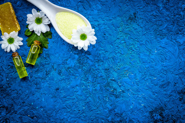 Chamomile spa cosmetics with natural herbal ingredients. Chamomile spa salt, soap, oil on blue background top view copy space